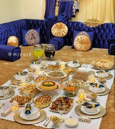 a table filled with lots of food on top of a carpeted floor next to blue couches