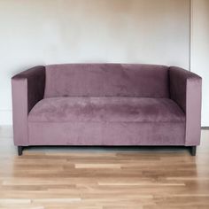 a purple couch sitting on top of a hard wood floor next to a white wall