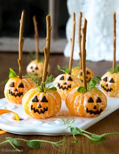 small pumpkins with sticks sticking out of them sitting on a white plate next to green leaves