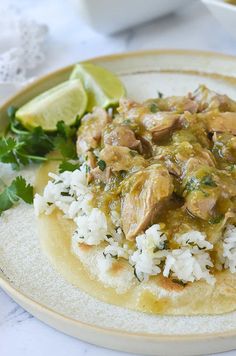 a plate with rice, meat and cilantro on it next to a lime wedge