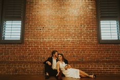 a man and woman sitting on the floor in front of a brick wall