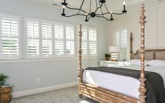 a bedroom with white walls and wooden bed frame in the center, along with windows that have shutters on both sides