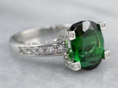 "Like the Northern Lights over mountains of glittering ice, the green of this tourmaline gemstone is simply breathtaking. Precision faceting brings out the shine of this intense tourmaline, allowing the more ethereal tones of green to gleam from deep within the stone. Set in polished platinum, encrusted with high-quality diamond creating bright flashes that perfectly accent the rich shade of evergreen that is the main theme of the stone. We've set this beautiful green tourmaline into a versatile Ring Green Stone, Yellow Gold Sapphire Ring, Demantoid Garnet, Green Stone Rings, Diamond Cocktail Ring, Main Theme, The Northern Lights, Diamond Cocktail Rings, Tourmaline Ring