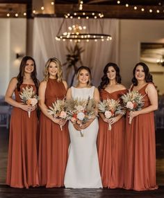 a group of women standing next to each other holding bouquets in front of a chandelier