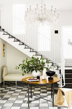 a living room filled with furniture and a chandelier hanging from the side of a stair case