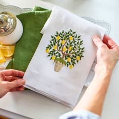 a woman is working on an embroidered dish towel with lemons and a potted tree