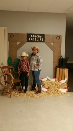 two people standing next to each other in front of a fake barn and hay pile