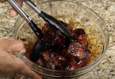 someone using tongs to stir meat in a glass bowl on the counter with other food items