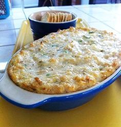 a casserole dish on a yellow table next to a bowl of crackers