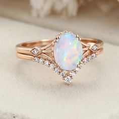 a white opal and diamond ring set on top of a cloth with flowers in the background