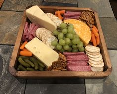 an assortment of cheeses, crackers, and meats in a wooden tray