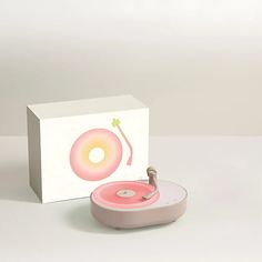 a pink record player sitting on top of a white table next to a cardboard box