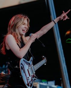 a woman holding a guitar and pointing to something in the air with her right hand