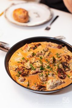 a pan filled with food sitting on top of a white table next to silverware