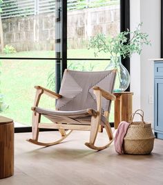 a rocking chair next to a window with a basket and vase on the floor in front of it