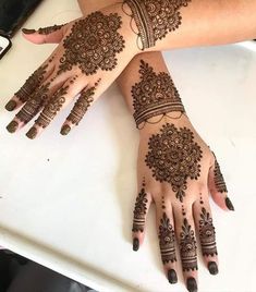 two hands with henna tattoos on them, one is showing off the intricate design