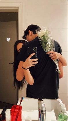 a man and woman embracing each other in front of a mirror with flowers on it