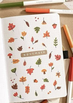 an open notebook with autumn leaves and the word november written on it, surrounded by pencils