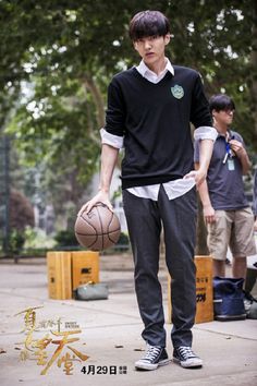 a young man holding a basketball while standing next to another person on a sidewalk with trees in the background