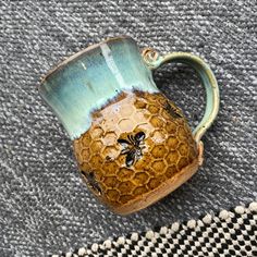 a blue and yellow mug with a bee on it sitting on top of a rug