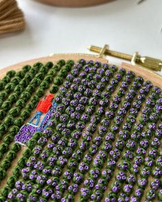 a close up of a cross stitch pattern on a wooden hoop with purple and green flowers