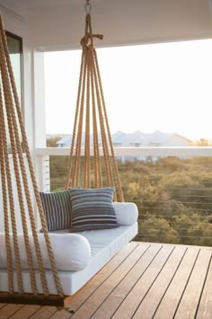 a white couch sitting on top of a wooden floor next to a swing chair with pillows