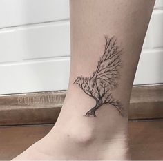 a small tree tattoo on the ankle is shown in black and grey ink, with branches growing out of it