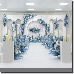 a white room with blue flowers and candles on the floor, surrounded by pillars that are decorated with wreaths