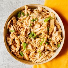 a bowl filled with shredded chicken and garnished with green onions on a yellow cloth