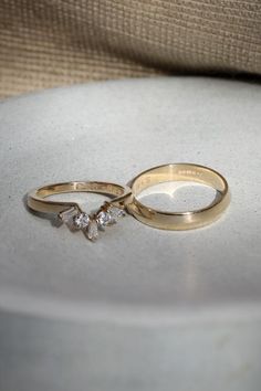 two gold wedding rings sitting on top of a white plate