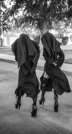 two people in black clothing walking down the street with their backs turned to one another