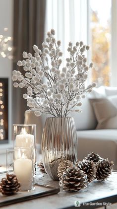 a glass vase filled with white flowers and pine cones on top of a coffee table