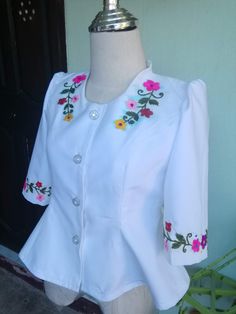 a white blouse with colorful flowers on the collar and sleeves, sitting on a mannequin