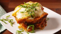 a white plate topped with lasagna covered in cheese and green onions on top of a wooden table