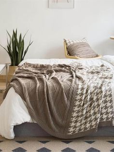 a bed with a blanket on top of it next to a potted plant in the corner