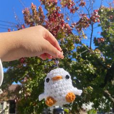 a hand is holding a small crocheted bird ornament in front of a tree