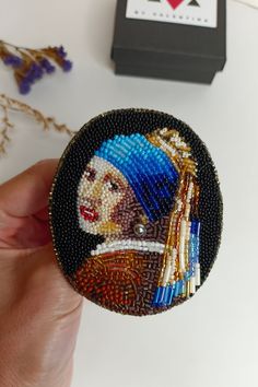 a hand holding a beaded button with a painting on it