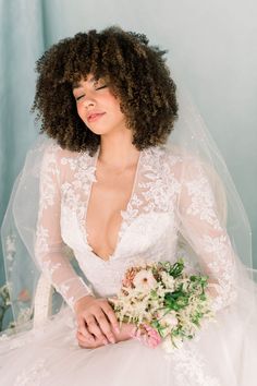 a woman in a wedding dress sitting on a chair with her hair down and holding a bridal bouquet