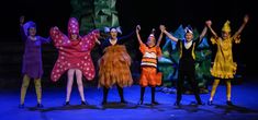 five people in costumes standing on stage with their hands up and one person wearing a costume