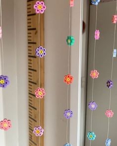 colorful paper flowers hanging from strings in front of a wall with a ruler on it