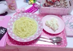 a pink table topped with plates of food and utensils next to a hello kitty lunch box