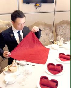 a man sitting at a table holding up a piece of red cloth with hearts on it