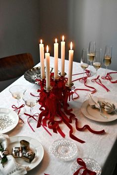 a table topped with white plates covered in red ribbon next to wine glasses and candles