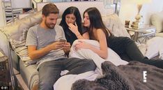 two people sitting on a bed looking at a cell phone while the woman is holding a baby