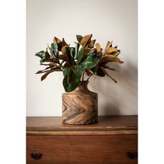 a wooden vase filled with green leaves on top of a dresser next to a white wall