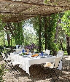 an outdoor dining area with tables and chairs under a pergolated roof, surrounded by greenery