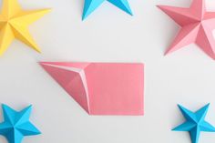 three origami stars and one folded paper star on a white surface with pink, blue, and yellow colors