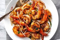 a white plate topped with shrimp and onions on top of a table next to a fork