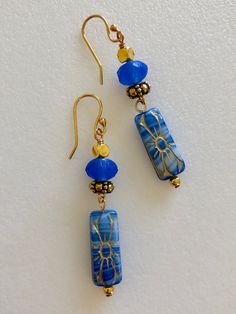 "Beautiful marbled blue denim Czech flower beads accented with golden bronze. 20 x 8 mm pressed glass rectangles. Topped with cornflower blue Czech sea glass beads. 8 x 6 mm matte blue rondelles. Ornate antique gold beaded spacers and cube accents. Gold plated French ear hooks. Total drop 2\"." Artisan Blue Beaded Earrings, Blue Earrings With Spacer Beads For Gift, Artisan Blue Jewelry With Gold Beads, Blue Earrings With Gold Beads, Artisan Blue Beaded Earrings As Gift, Bohemian Blue Earrings With Gold Beads, Denim Earrings, Aquamarine Earrings, Flower Beads