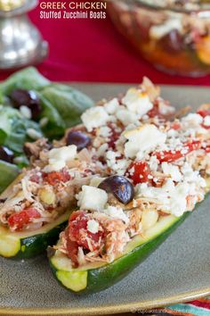 stuffed zucchini boats on a plate with lettuce, olives and cheese